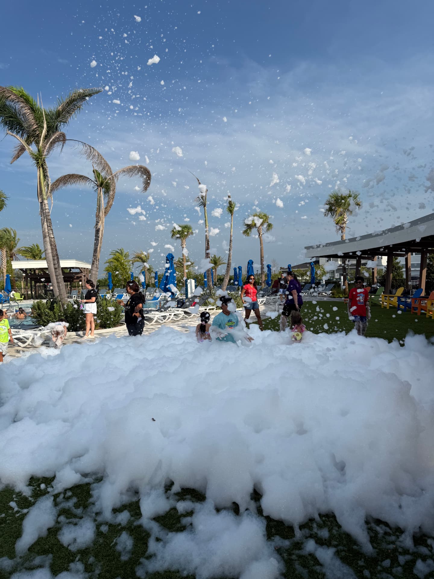Foam plume shooting into a blue sky over a pool deck packed with kids