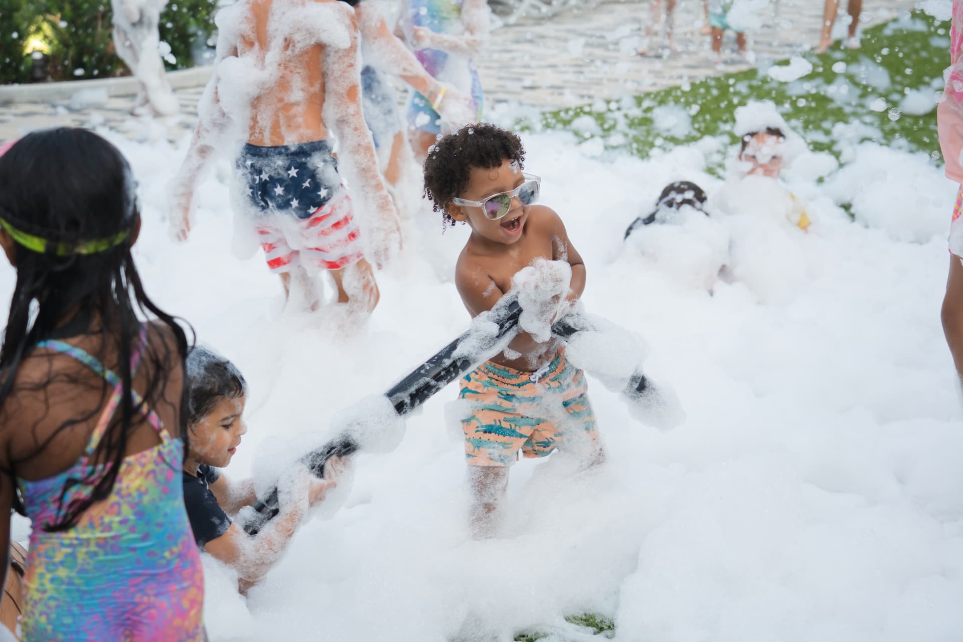 Kids playing with a foam blaster tube in knee deep foam at a community foam party