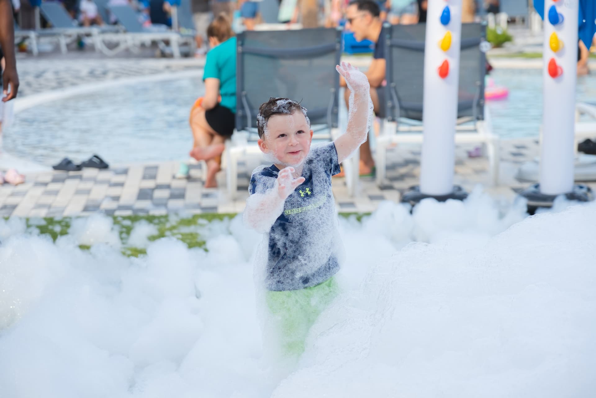 Child waving with foam covered hands beside a pool