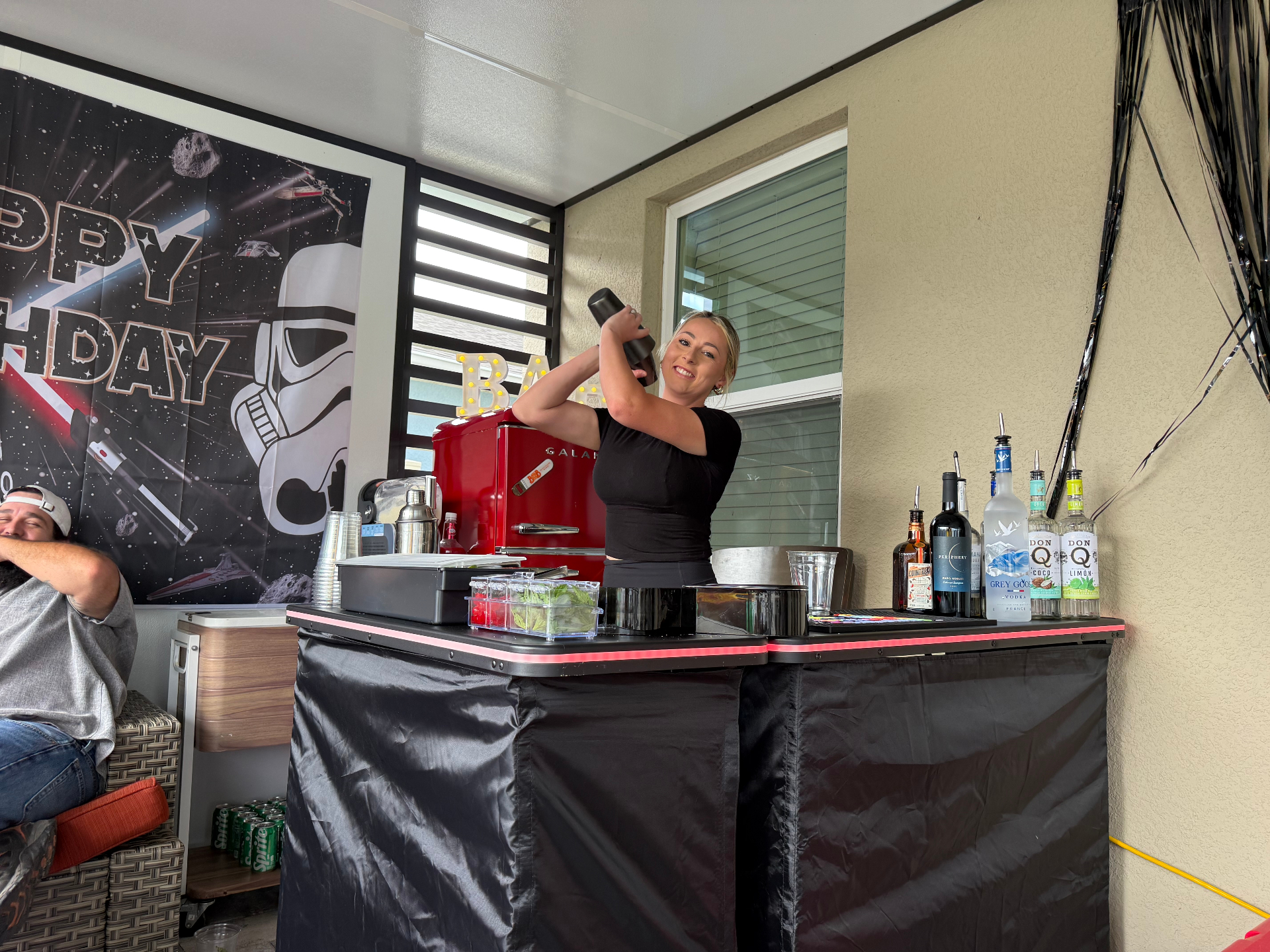 Independent bartender shaking a cocktail behind a black LED mobile bar setup at a themed adult birthday party