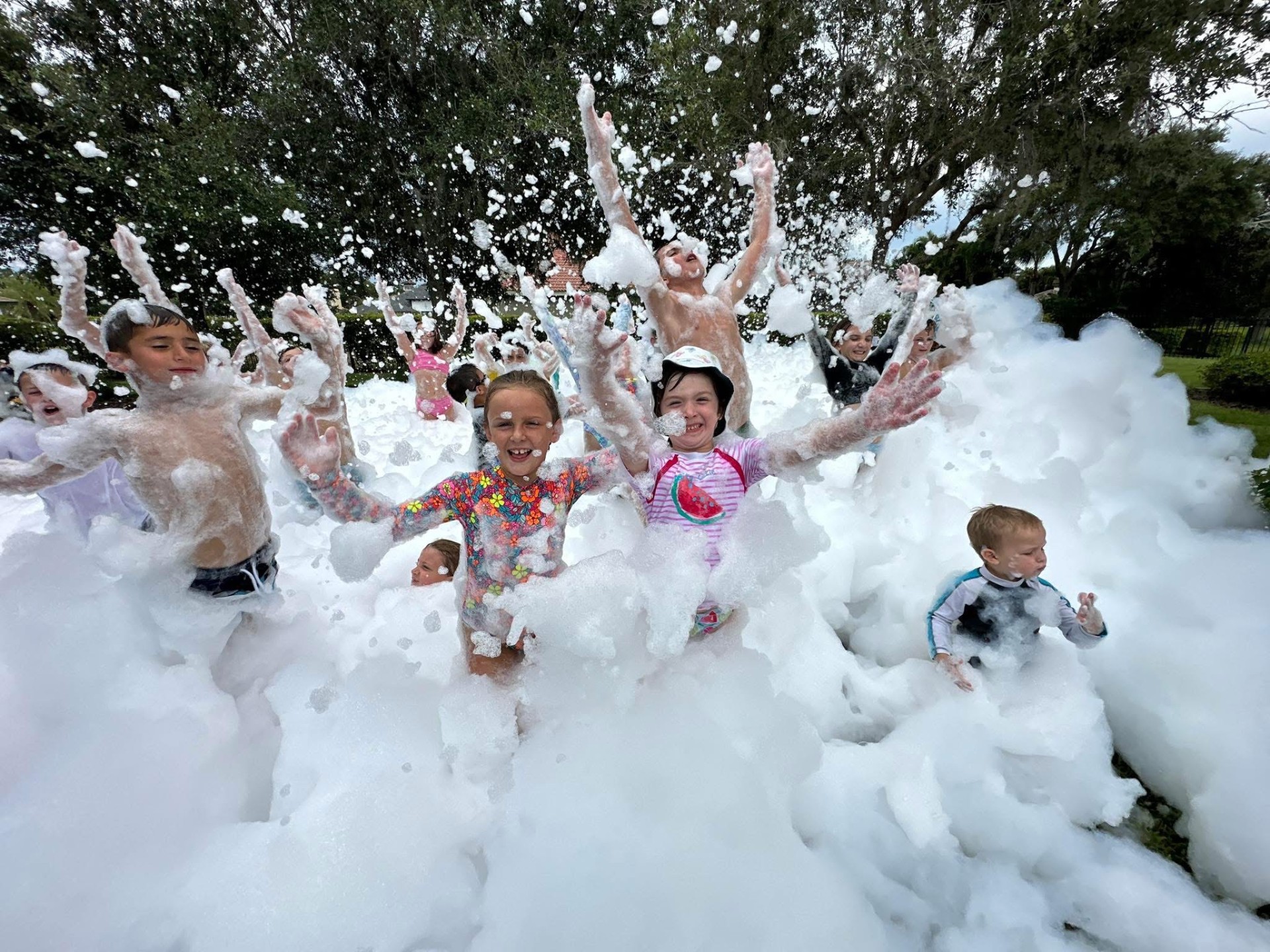 A crowd of kids throwing their hands in the air, buried waist deep in foam at a backyard foam party