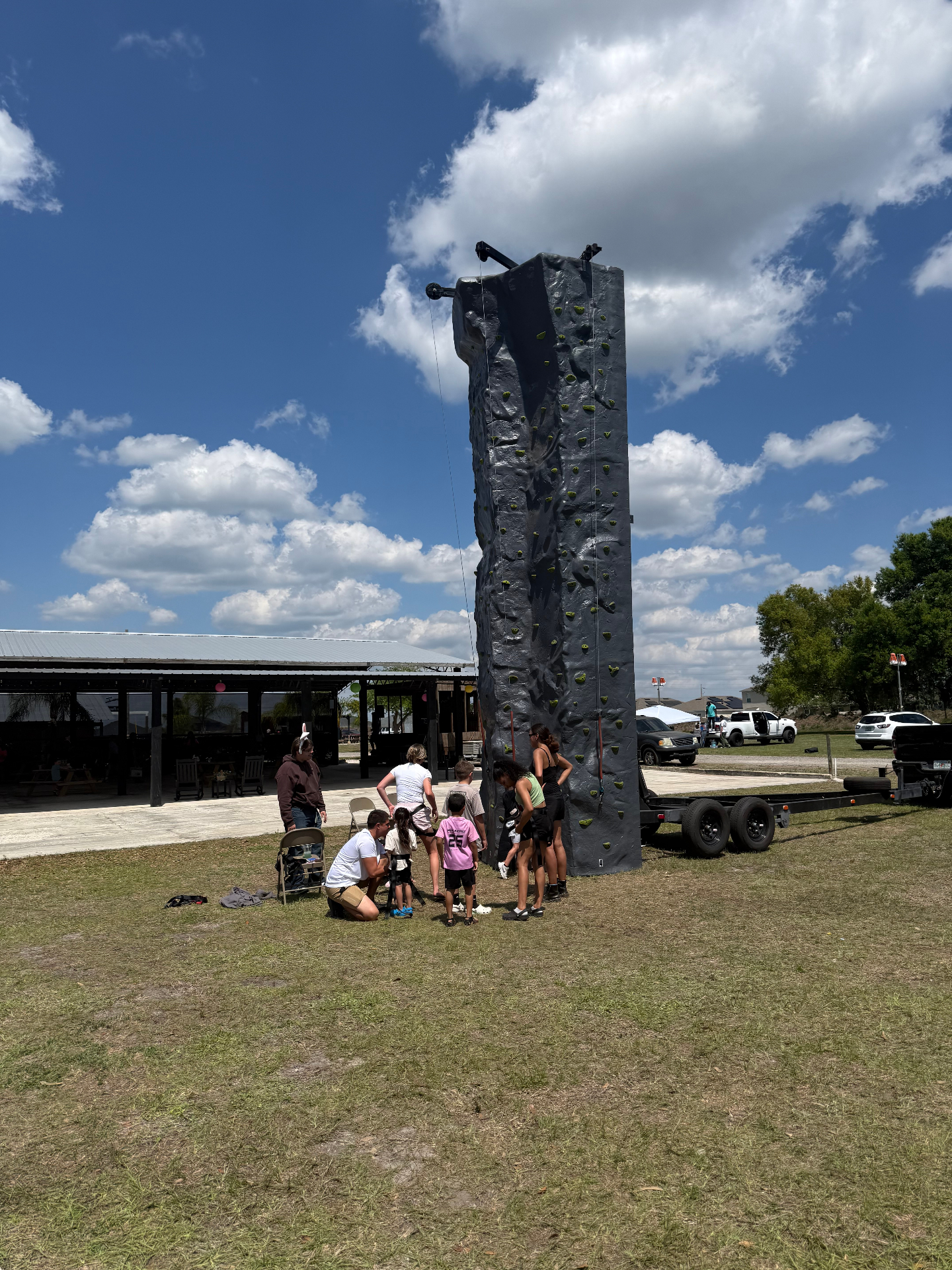 Trailer mounted 24 foot rock climbing wall set up at an outdoor event with kids gearing up to climb